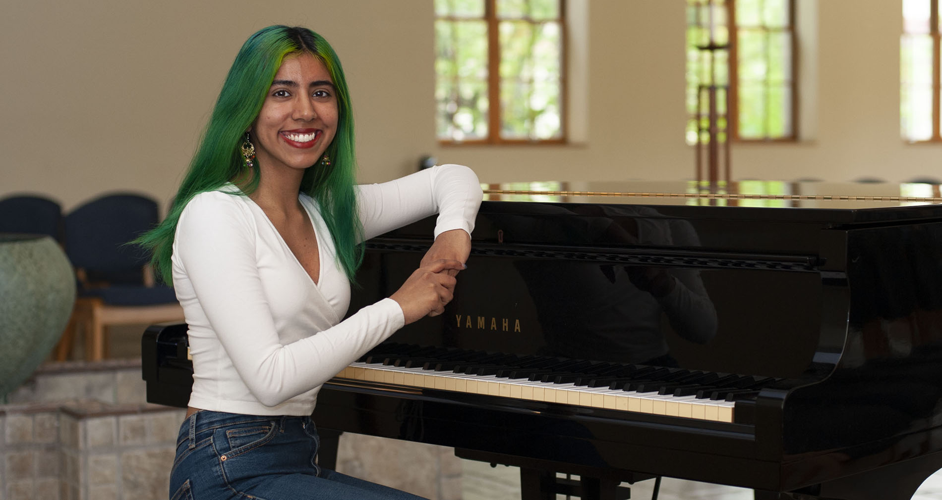 Mehar Soni sits smiling next to a piano inside of the St. Ignatius Chapel.