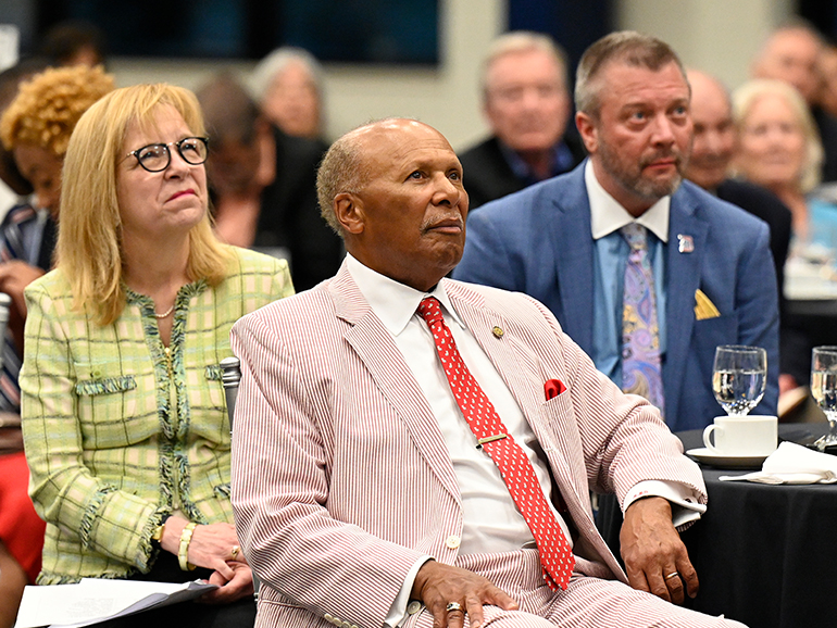 Three Detroit Mercy administrators sit around a table and watch a video being played.