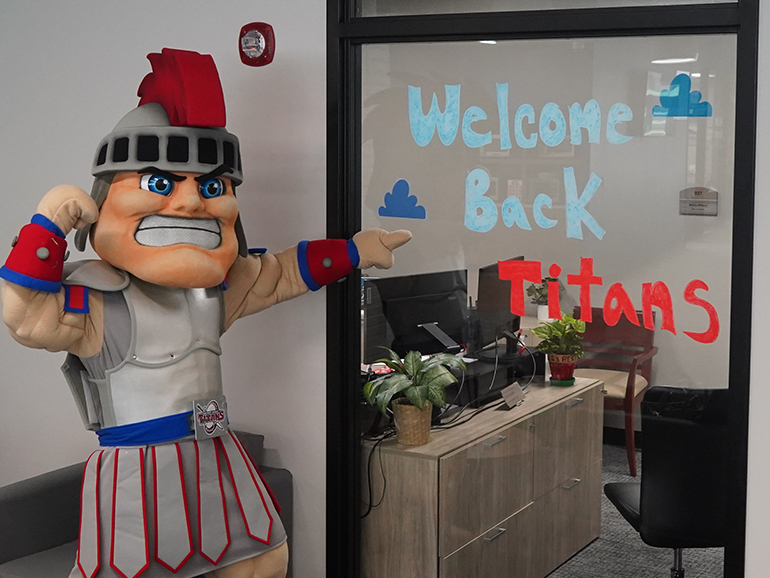 Tommy Titan points to a sign on a window inside of the Student Union that reads, Welcome Back Titans.