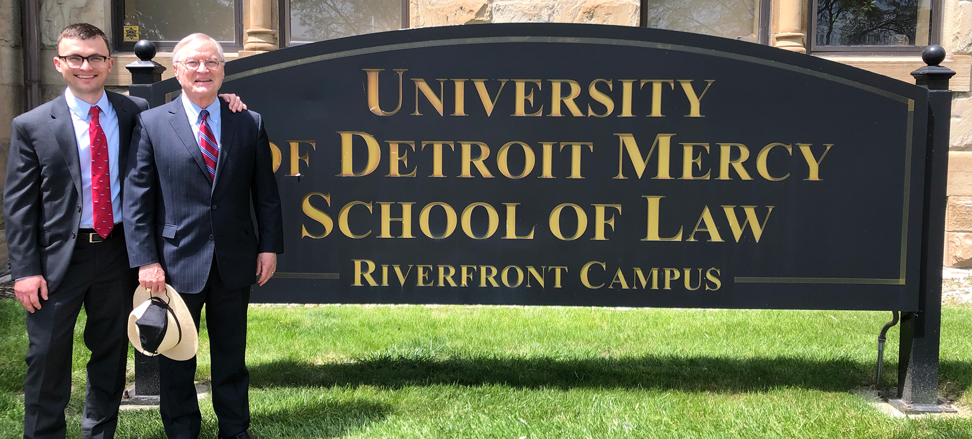 Kevin Lynch stands next to his father and the Detroit Mercy School of Law Riverfront Campus sign during a campus tour.