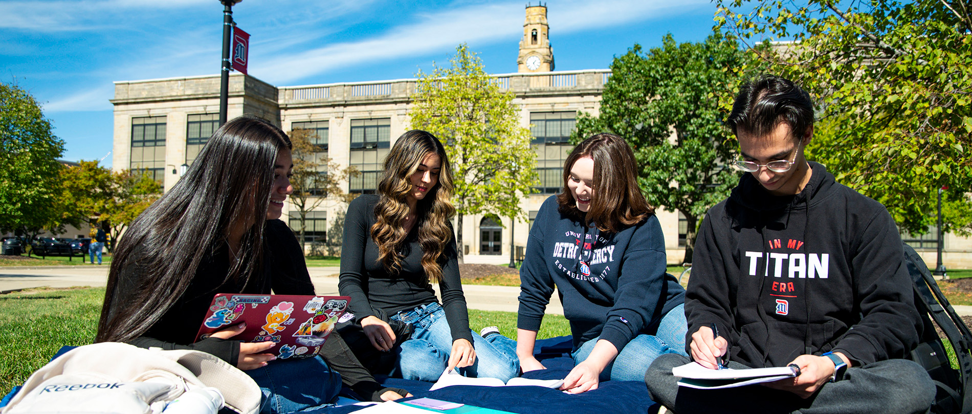 Four students sit and socialize on the grass of the McNichols Campus.