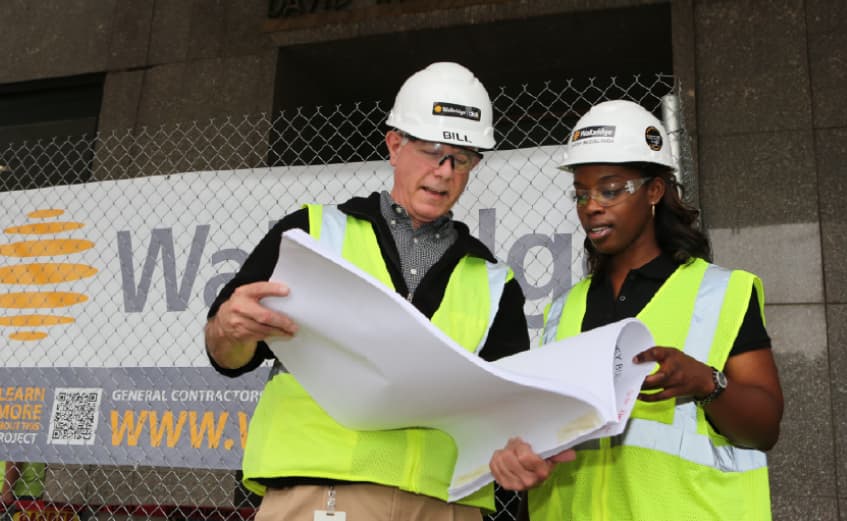 older man in a hard hat at walbridge showing student intern some plans