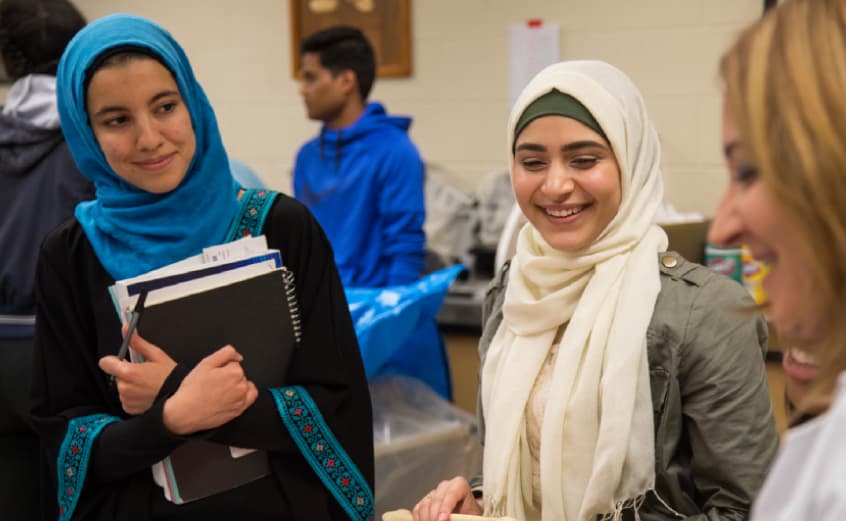 two female students wearing hijabs talking to a bio professor