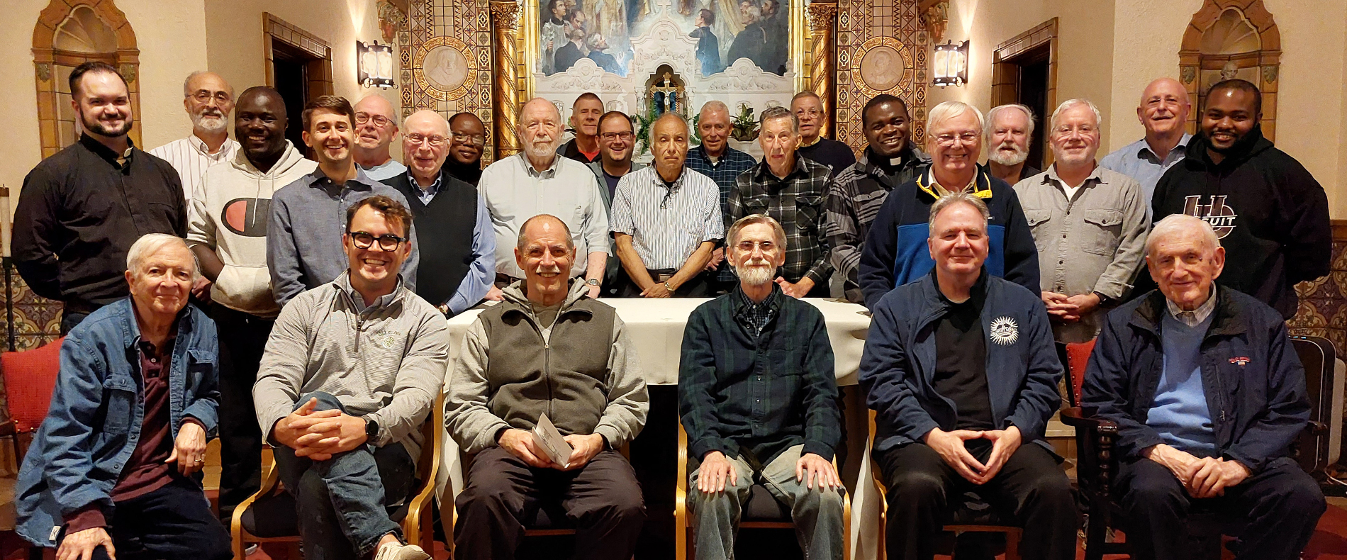 The Detroit Jesuit Community, featuring more than two dozen people sitting and standing inside of a church.