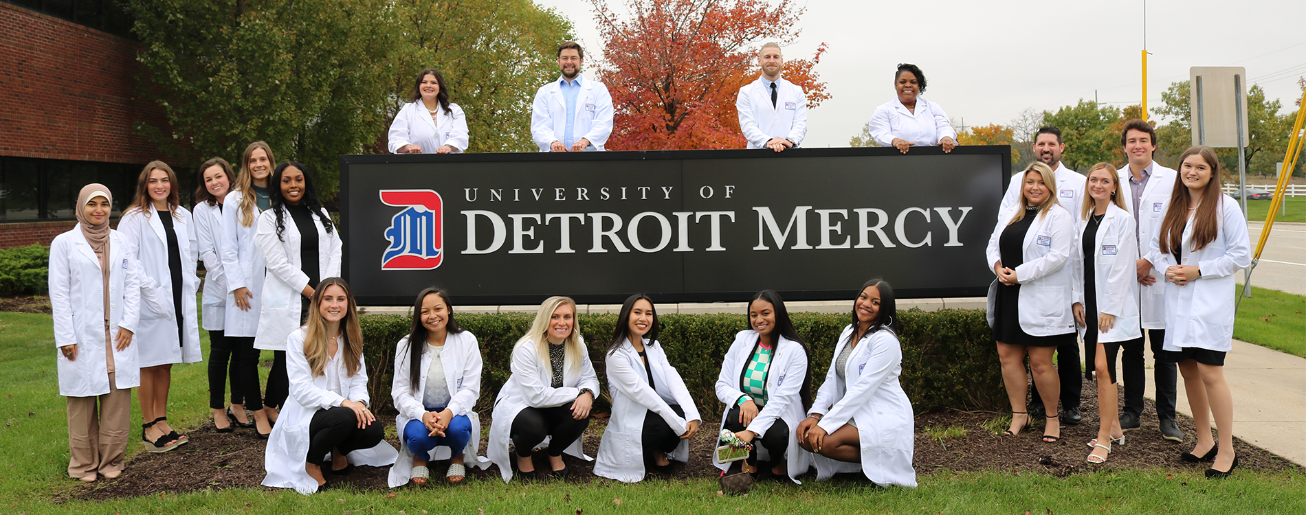 Twenty MEAGN students stand outside of the Novi campus surrounding the big University of Detroit Mercy sign.
