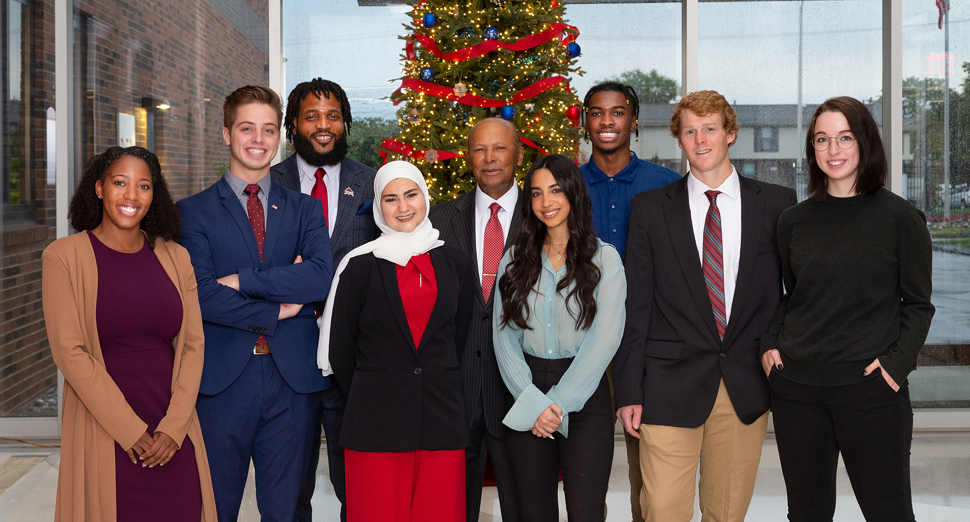 Detroit Mercy's Christmas card photo, featuring President Antoine M. Garibaldi and several students posing in front of a Christmas tree.