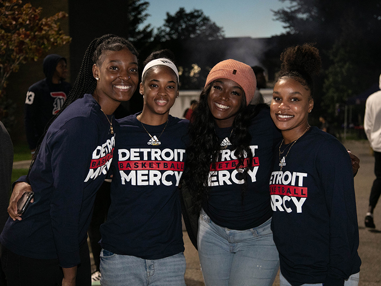 A group of female students wearing Detroit Mercy basketball shirts pose for a photograph during Homecoming.