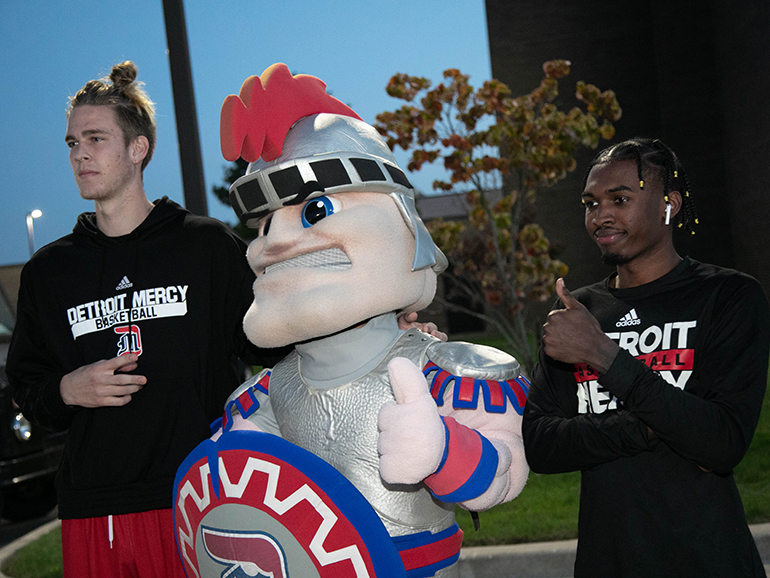 Two Detroit Mercy men’s basketball players pose for a photo with Tommy Titan.
