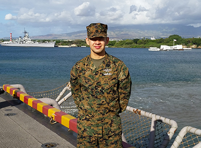 A photo of Renso Sanchez standing on a military ship. In the background, more ships can be seen