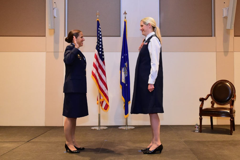 Two people perform a military promotion ceremony while facing each other indoors.