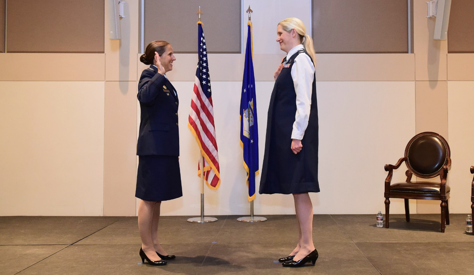 Two people perform a military promotion ceremony while facing each other indoors.