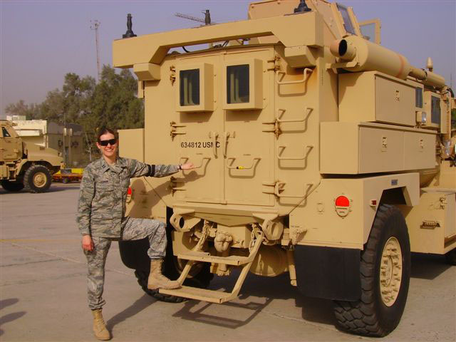 One person poses for a photo next to a tan humvee while outdoors.