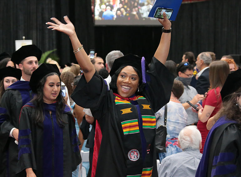 A Law graduate celebrates at the end of commencement by raising her hands and smiling.