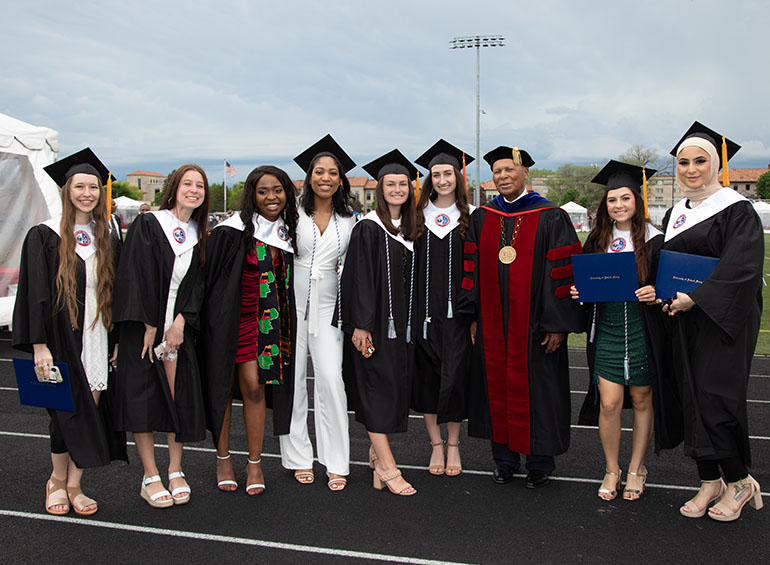 A group of female graduates pose for a photo with President Garibaldi on the Titan Field track.