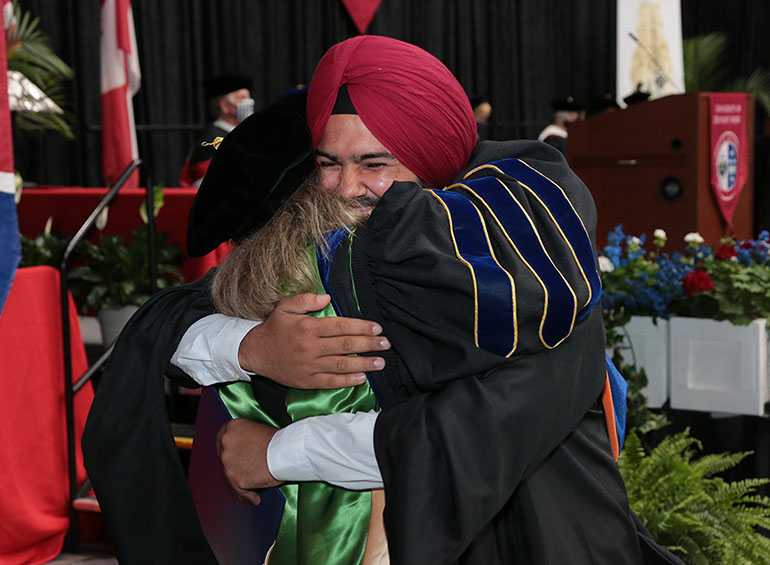 A graduate hugs an administrator in celebration after receiving his degree during commencement.