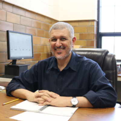 Professor Nihad Dukhan smiles for a photograph while sitting at a desk in his office.