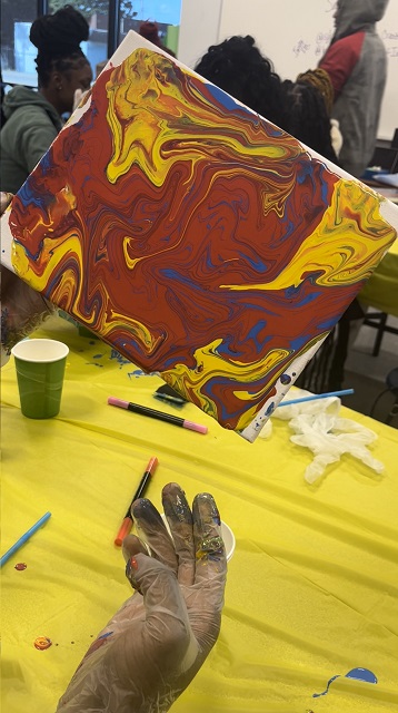 A person holds up a painted canvas during an event held indoors.