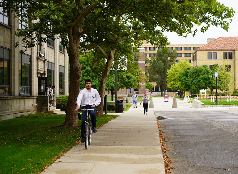 A student rides his bike on the sidewalk near the Engineering Building while other students walk around campus during the first day of classes.