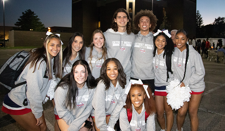 A dozen member of the Detroit Mercy cheer team pose for a photo outdoors.