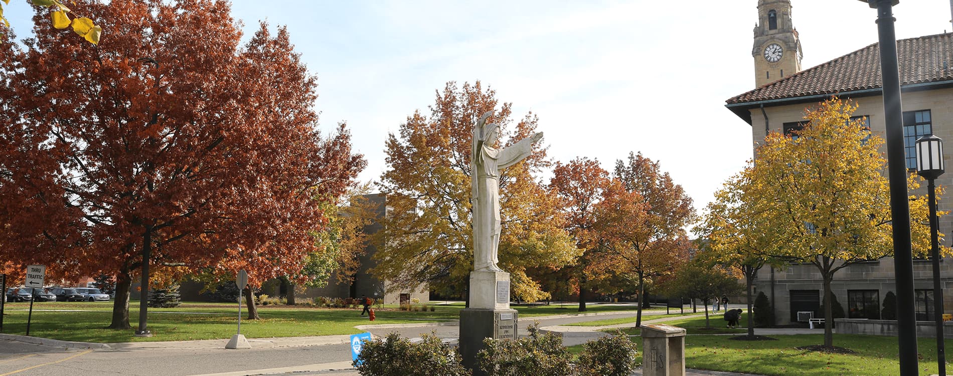 A photo of the Jesus statue on the McNichols Campus, with the Clocktower and students visible in the background.