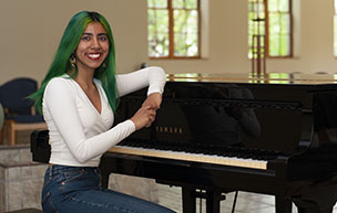 Mehar Soni sits smiling at a piano inside of the St. Ignatius Chapel.