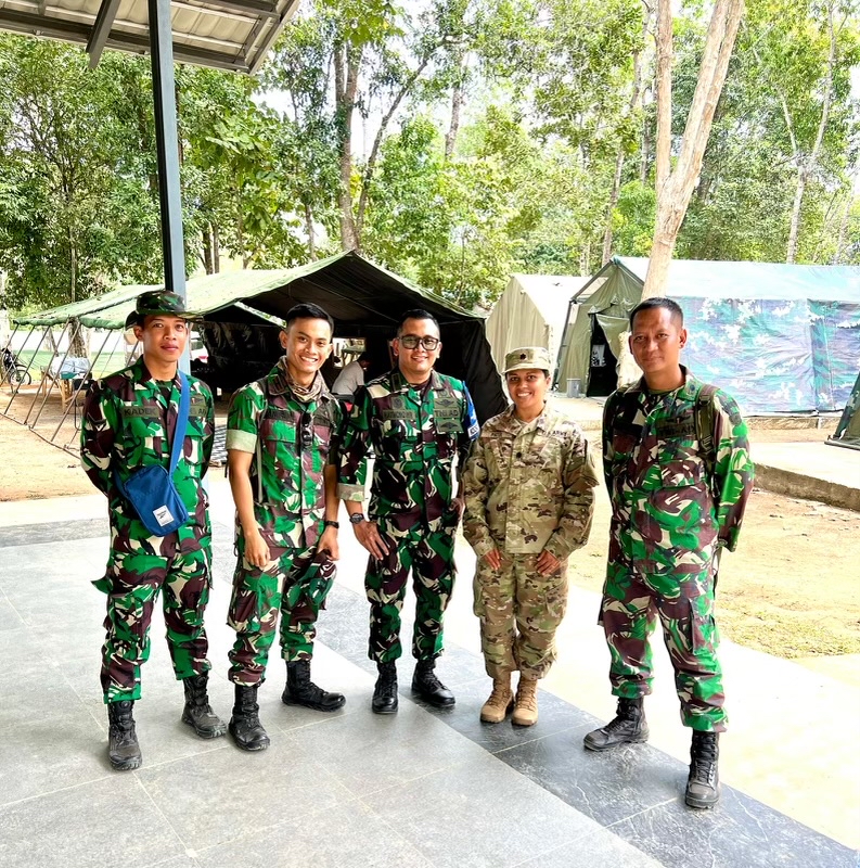 Five people, in camouflage attire, stand outside and smile for the camera.