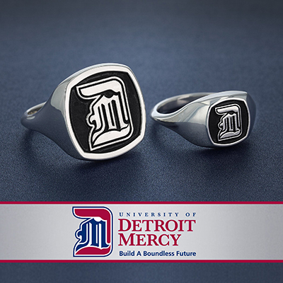 The image shows two rings, one large and one smaller with the University of Detroit Mercy logo etched into the faces of both.  The rings are laying on a black table top and a graphic banner with the words "University of Detroit Mercy, Build a Boundless Future" written below.