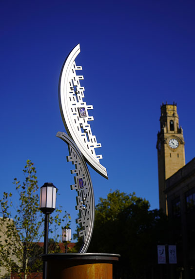 A photo of the unnamed sculpture on the McNichols Campus, with the clocktower in the background.