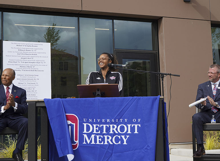 A student speaks during the grand opening and blessing of the new Student Union. The student is standing between Antoine M. Garibaldi and Donald B. Taylor, who are both seated near the table.