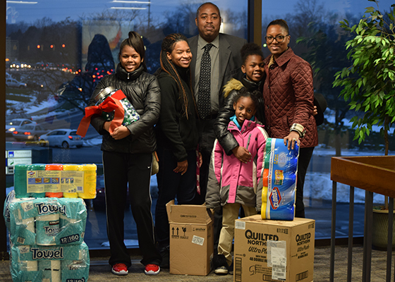 Multiple people pose for a photo surrounded by donations of paper towels and cleaning supplies.