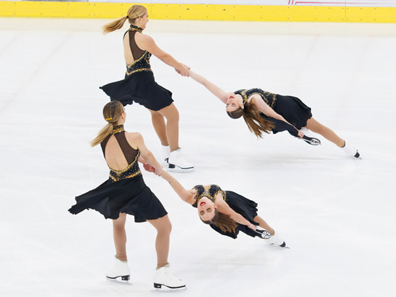Four synchronized skaters skate on ice.