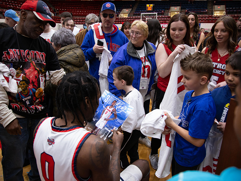 Antoine Davis sits in a chair and signs autographs surrounded by more than two dozen people.