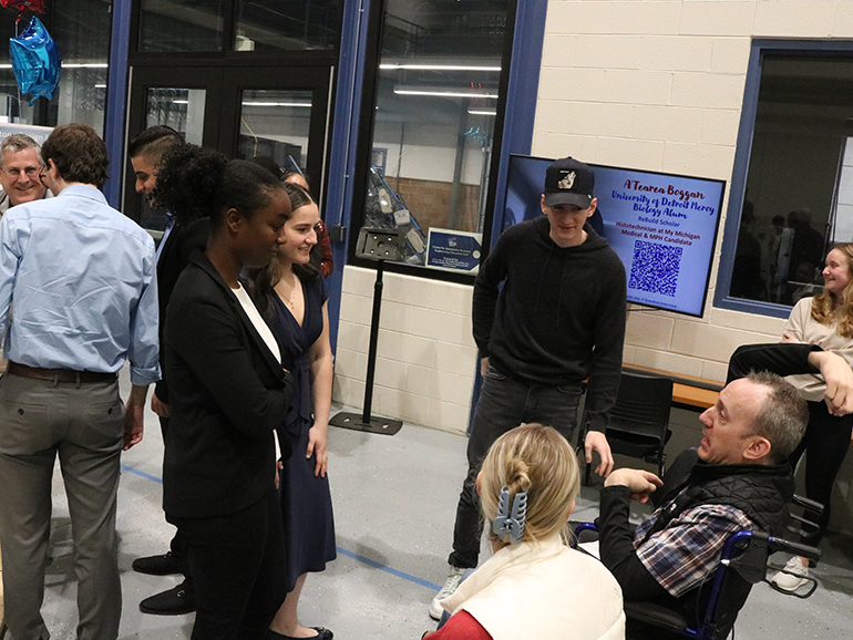 People stand and sit and talk to one another inside of the High Bay in the College of Engineering.