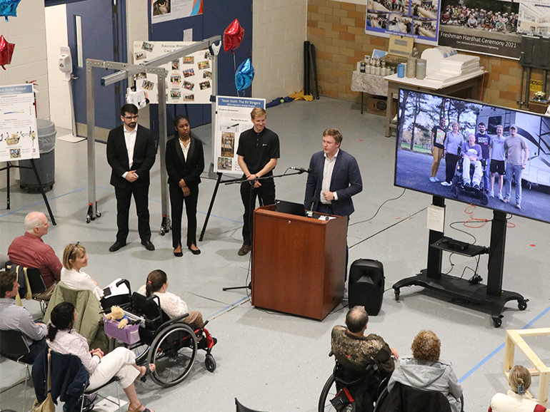 Four students present their project to people sitting in front of them inside of the High Bay of the College of Engineering.