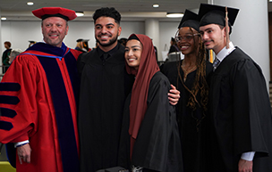 Five people standing in robes inside of a building and smiling.