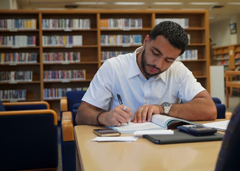 One person sits at a table while reading and writing.