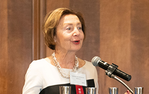 Kathy Dul Aznavorian speaking from a podium, with a red, white and blue University of Detroit Mercy banner hanging from it.