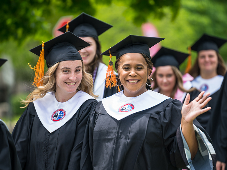 Graduates smile and wave as they walk to Calihan Hall for commencement.