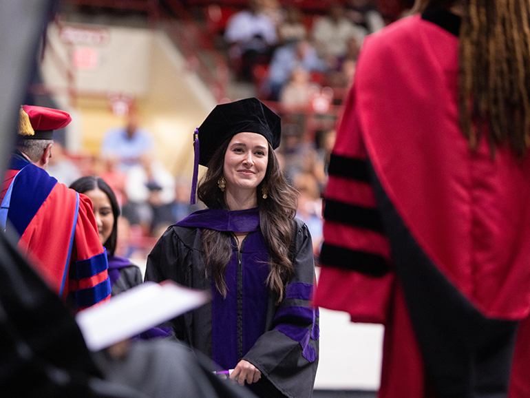 A graduate smiles as she walks across the stage to interact with Dean Jefferson Exum during commencement.