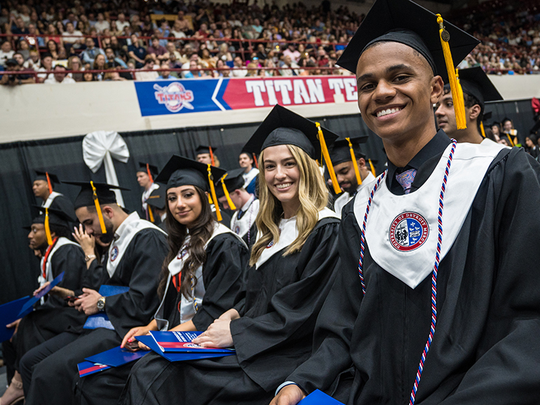 Graduates smile for a photo as other graduates line up to walk across the stage beneath the Titan Territory sign.