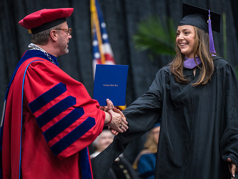 A graduate shakes President Taylor’s hand as she walks across the stage at commencement.