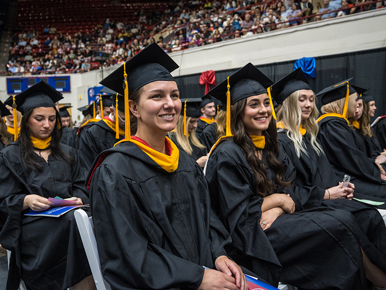 Graduates smile and follow along during commencement.