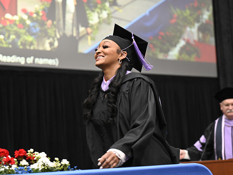 A graduate smiles as she walks across the stage at commencement.