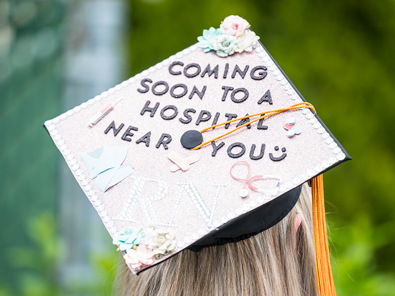 A graduation cap is decorated in pink stones with flowers, a stethoscope and nursing gear with the text: “Coming soon to a hospital near you, RN.”