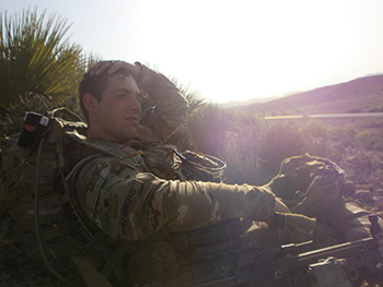 David Shears touches the top of his head while sitting down outside in his military uniform.