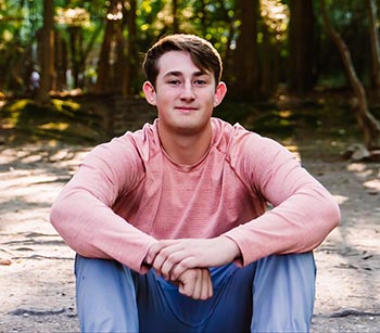 Devin Wouters poses for a photo while sitting down amongst some trees.