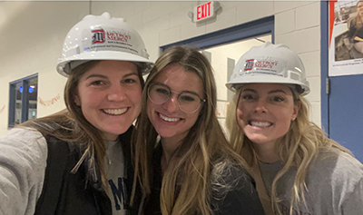 Kirstin Finnila and two of her friends take a selfie in the Engineering Building while wearing hard hats.