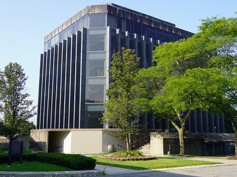 An exterior photo of the Fisher Building on a sunny day, with trees, flowers and bushes pictured in the foreground.