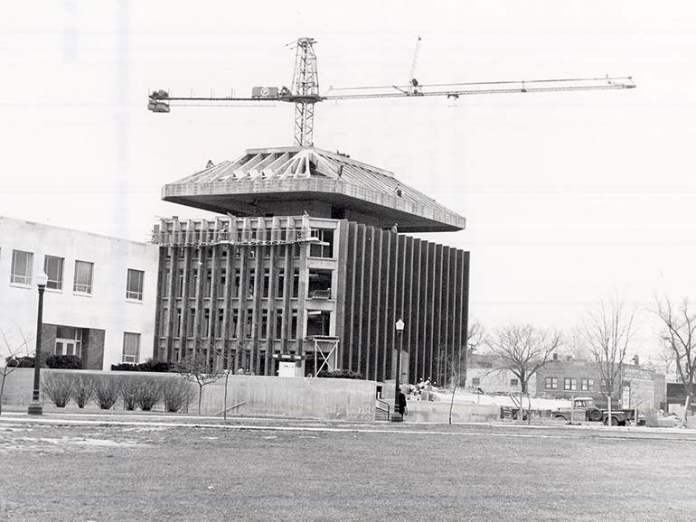A black and white photo shows a large crane behind the Fisher Building being constructed.