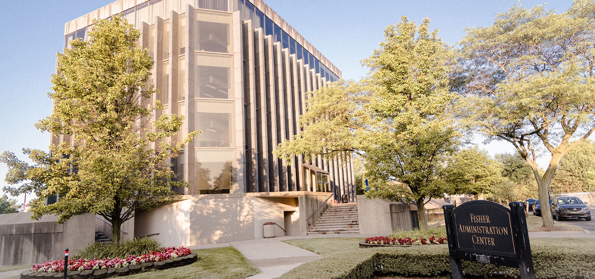 An exterior photo of the Fisher Administration Center, with flowers and trees seen in front of it on a sunny day.